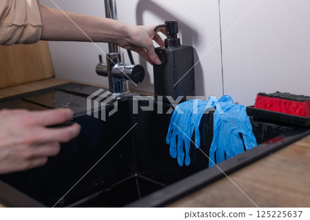 A Close-Up View of Cleaning Supplies and Tools in a Modern Kitchen Workspace with Blue Gloves and Soap Dispenser for Household Cleaning Tasks A Close-Up View of Cleaning Supplies and Tools in a Modern Kitchen Workspace with Blue Gloves and Soap Dispenser for Household Cleaning Tasks 125225637