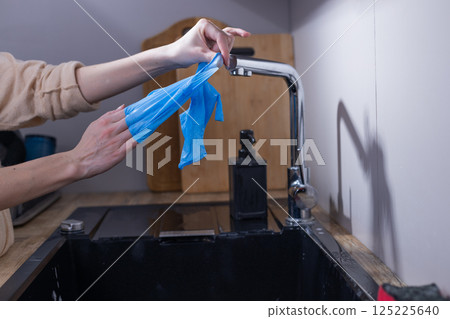 A Person Using Blue Disposable Gloves While Preparing to Wash Dishes, Promoting Hygiene and Cleanliness in a Modern Kitchen Environment 125225640