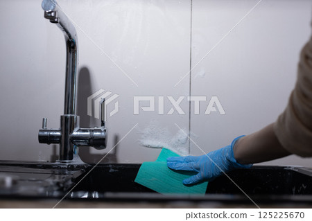 Cleaning a Kitchen Sink: A Close-Up of a Hand Scrubbing with a Sponge in a Modern Kitchen Environment Focused on Hygiene and Cleanliness 125225670