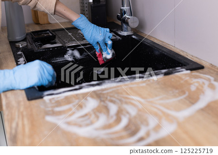 Detailed Image of Hands Cleaning a Kitchen Sink with Soap and Gloves, Showcasing Home Care Practices in a Modern Kitchen Setting for Hygiene and Cleanliness Detailed Image of Hands Cleaning a Kitchen Sink with Soap and Gloves, Showcasing Home Care Practices in a Modern Kitchen Setting for Hygiene and Cleanliness 125225719