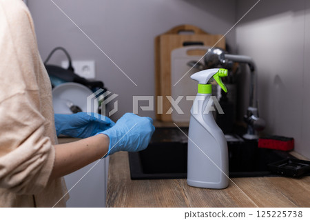 Essential Kitchen Cleaning Supplies: A Person in Blue Gloves Prepares to Use a Spray Bottle for Effective Disinfection on a Wooden Countertop Essential Kitchen Cleaning Supplies: A Person in Blue Gloves Prepares to Use a Spray Bottle for Effective Disinfection on a Wooden Countertop 125225738