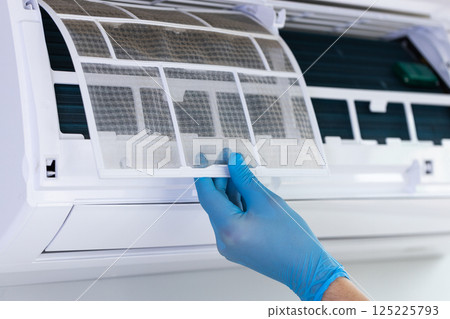 Detailing the Maintenance Process: Carefully Removing a Dusty Air Conditioner Filter with Gloved Hands for Efficient Cleaning and Optimal Performance Enhancement 125225793