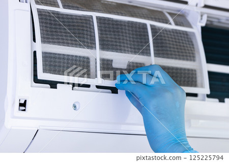 An Individual Maintaining the Air Conditioning Unit: Removing the Filter for Cleaning and Maintenance to Ensure Efficient Cooling and Air Quality Inside the Home Environment 125225794