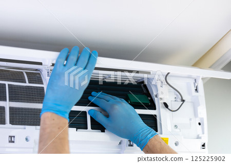 Technician Performing Maintenance on Air Conditioning Unit Wearing Disposable Gloves to Ensure Cleanliness and Prevent Contamination While Installing or Cleaning Filters 125225902