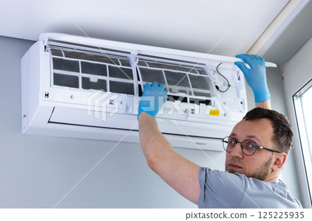 Professional HVAC Technician Performing Maintenance on Air Conditioner Unit Inside a Modern Room for Improved Indoor Air Quality and Efficiency in Home Cooling Solutions Professional HVAC Technician Performing Maintenance on Air Conditioner Unit Inside a Modern Room for Improved Indoor Air Quality and Efficiency in Home Cooling Solutions 125225935