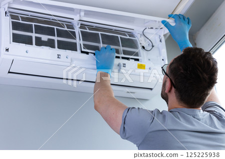 Individual Performing Routine Maintenance on Air Conditioning Unit While Wearing Blue Gloves, Ensuring Clean and Efficient Operation for Comfortable Indoor Environment 125225938