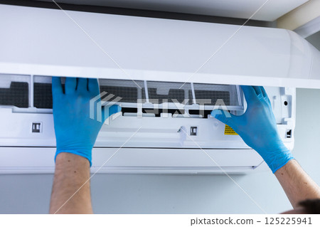 An Individual Performing Maintenance on an Air Conditioning Unit: Cleaning the Filter for Improved Performance and Efficiency in Indoor Air Quality An Individual Performing Maintenance on an Air Conditioning Unit: Cleaning the Filter for Improved Performance and Efficiency in Indoor Air Quality 125225941
