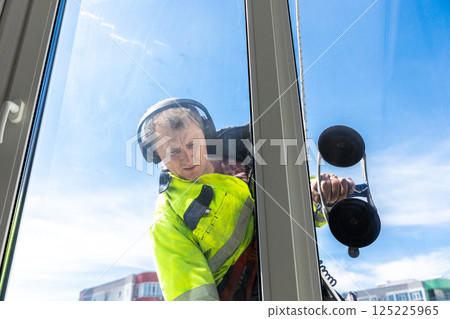 Dedicated Window Cleaner Man with Headphones Cleaning Big Glass Window in Bright Sunny Day Overlooking Cityscape, Ensuring Transparency and Clarity for Building Residents and Passersby Dedicated Window Cleaner Man with Headphones Cleaning Big Glass Window in Bright Sunny Day Overlooking Cityscape, Ensuring Transparency and Clarity for Building Residents and Passersby 125225965