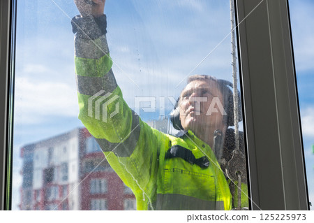 Professional Window Cleaner in Safety Gear Cleaning Glass to Ensure Crystal Clarity in High-Rise Building Under Bright Sunny Sky with Clear View of Urban Environment Professional Window Cleaner in Safety Gear Cleaning Glass to Ensure Crystal Clarity in High-Rise Building Under Bright Sunny Sky with Clear View of Urban Environment 125225973