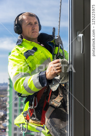 Professional Window Cleaner Engaged in Safe High-Rise Cleaning Using Safety Gear and Tools for Optimal Performance in Urban Environment Professional Window Cleaner Engaged in Safe High-Rise Cleaning Using Safety Gear and Tools for Optimal Performance in Urban Environment 125225975
