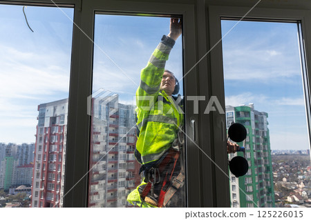 High-Elevation Window Cleaner Performing Cleaning Tasks on a Residential Skyscraper, Wearing Safety Gear to Ensure Well-Being While Maintaining Clean Glass Surfaces 125226015