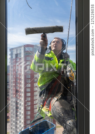 Professional Window Cleaner Working at Heights with Safety Gear and Equipment, Showing Expertise in High-Rise Cleaning While Ensuring Safety and Quality Standards on a Sunny Day 125226038