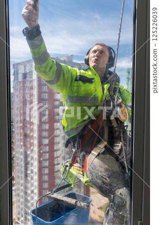 An Engaged Window Cleaner at Work on a High-Rise Building, Safely Washing Windows and Utilizing Protective Gear for Optimal Performance and Safety Procedures 125226039