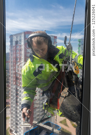 Professional Window Cleaner Performing Cleaning and Maintenance on Skyscraper's Windows Using Safety Gear for Protection Against Heights and Environmental Conditions 125226041