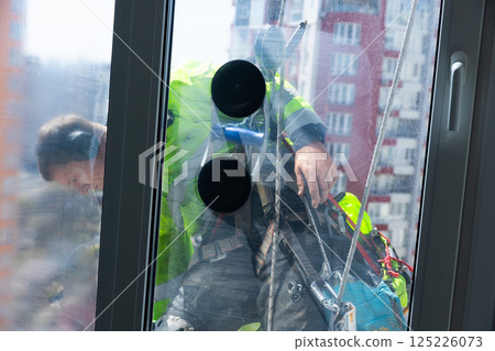 A Professional Window Cleaner at Work: The View from Inside a High-Rise Building Captured Through a Glass Panel During a Bright Sunny Day in an Urban Setting A Professional Window Cleaner at Work: The View from Inside a High-Rise Building Captured Through a Glass Panel During a Bright Sunny Day in an Urban Setting 125226073