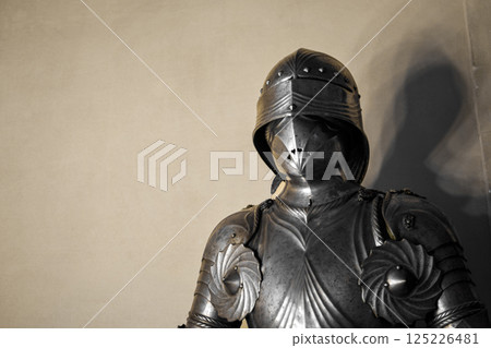 Front view of medieval shiny armor with details and white wall in background. Front view of medieval shiny armor with details and white wall in background. 125226481