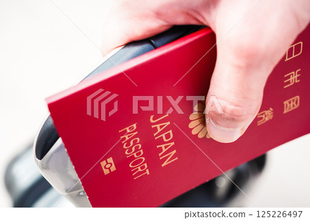 Close-up of a young man holding a passport with a boarding pass in it, carrying a suitcase and preparing to depart for a trip Close-up of a young man holding a passport with a boarding pass in it, carrying a suitcase and preparing to depart for a trip 125226497