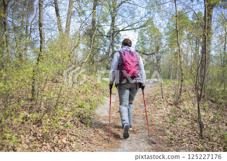A pensioner woman practicing Nordic walking in the forest A pensioner woman practicing Nordic walking in the forest 125227176