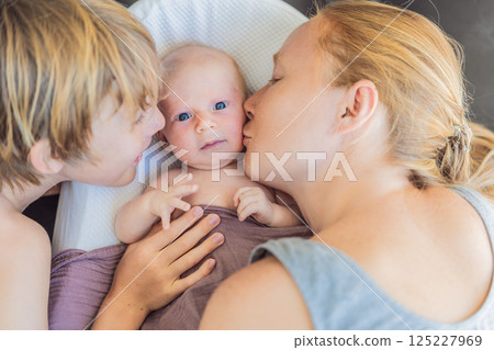 Mother and older son admiring their newborn baby in a cozy infant nest. Family bonding and sibling love concept Mother and older son admiring their newborn baby in a cozy infant nest. Family bonding and sibling love concept 125227969