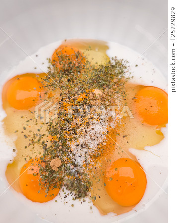 Raw eggs with spices and milk ready for whisking in a bowl Raw eggs with spices and milk ready for whisking in a bowl 125229829