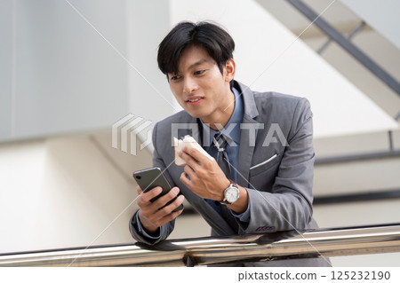 Young Asian businessman enjoying a snack while checking his phone in a modern office setting. Young Asian businessman enjoying a snack while checking his phone in a modern office setting. 125232190