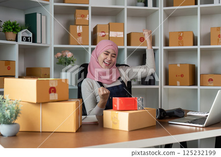 Excited Muslim woman celebrating success in her online business with packages. 125232199