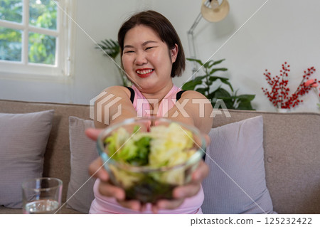 Overweight woman offering a fresh salad, promoting healthy weight loss. 125232422