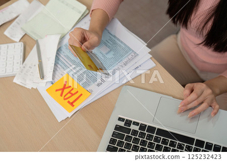Woman managing taxes with a credit card and financial documents on a desk. Woman managing taxes with a credit card and financial documents on a desk. 125232423