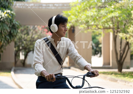 Joy of Cycling and Nature. Young man embracing cycling with headphones on in a green setting. 125232592