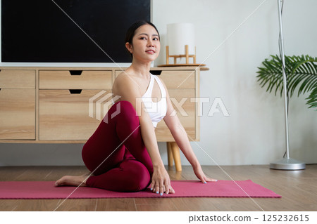 Yoga and Exercise. A woman demonstrating a yoga twist pose, enhancing flexibility and strength on a pink mat. 125232615