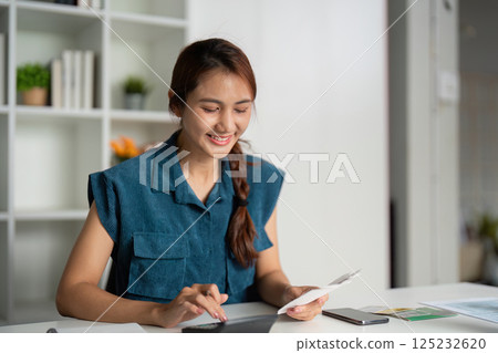 Budgeting and Financial Awareness. A smiling woman exploring her savings and payments on a tablet. Budgeting and Financial Awareness. A smiling woman exploring her savings and payments on a tablet. 125232620