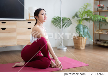 Yoga and Flexibility. A woman practicing the seated twist pose at home to enhance flexibility. Yoga and Flexibility. A woman practicing the seated twist pose at home to enhance flexibility. 125232668