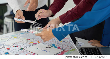 Collaboration and UX Design. Team members engaged in a collaborative UX design meeting, analyzing prototypes and sketching ideas together. 125232816