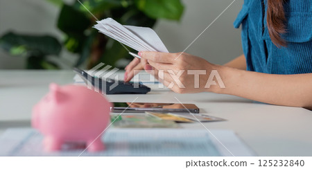 Savings and Budgeting Techniques. A person organizing bills while a piggy bank sits prominently on the table. 125232840