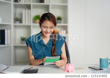 Smart Saving and Financial Tools. A delighted woman reviewing her finances while holding a sheet with savings. Smart Saving and Financial Tools. A delighted woman reviewing her finances while holding a sheet with savings. 125232905