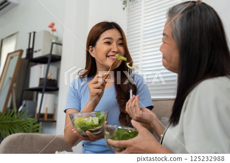 Nutrition and Joyful Moments. A daughter playfully feeds a mother with a healthy salad, reinforcing their family bond. Nutrition and Joyful Moments. A daughter playfully feeds a mother with a healthy salad, reinforcing their family bond. 125232988
