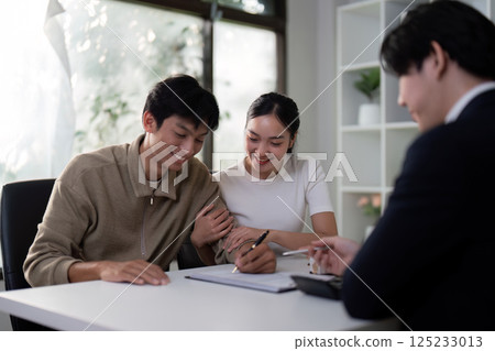 Finalization and Joy. A couple happily fills out paperwork with their agent during a real estate purchase. 125233013