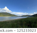 A tranquil lakeside scene surrounded by blue skies and mountains 125233023