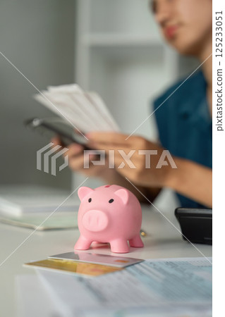 Financial Analysis and Management. An individual joyfully reviewing their savings strategy with a piggy bank in focus. Financial Analysis and Management. An individual joyfully reviewing their savings strategy with a piggy bank in focus. 125233051