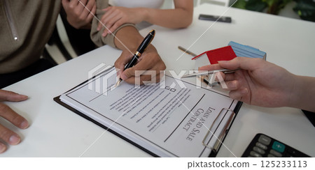 Real Estate and Contract Signing. A couple finalizing their home purchase agreement with a real estate agent. Real Estate and Contract Signing. A couple finalizing their home purchase agreement with a real estate agent. 125233113