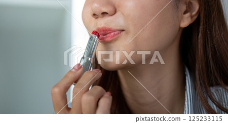 Beauty and Lip Application. A woman applying lipstick carefully, showcasing her focus and style. 125233115