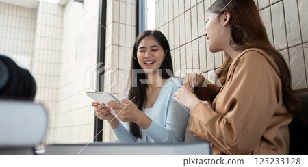 Joyful Sharing and Teamwork. Two friends happily discussing their projects with a tablet, showcasing collaboration and creativity. 125233128