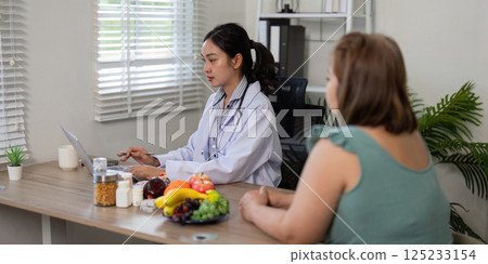 Nutritionist and Patient Interaction. A nutritionist works on a laptop during a productive consultation with a client about dietary habits and choices. Nutritionist and Patient Interaction. A nutritionist works on a laptop during a productive consultation with a client about dietary habits and choices. 125233154