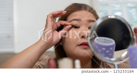Eye Makeup and Precision. A woman applying false eyelashes while looking in the mirror, focusing on her eye makeup. Eye Makeup and Precision. A woman applying false eyelashes while looking in the mirror, focusing on her eye makeup. 125233184