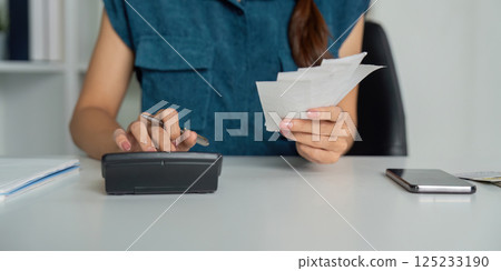 Smart Budgeting and Expense Management. A woman focused on organizing her finances using a calculator and handling receipts. 125233190