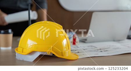 Safety and Planning. A yellow hard hat positioned on professional documents in an engineering workspace. Safety and Planning. A yellow hard hat positioned on professional documents in an engineering workspace. 125233204