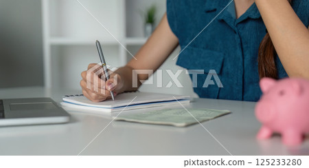 Smart Saving and Financial Insight. A woman analyzing her savings approach with a piggy bank nearby. 125233280