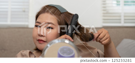 Hair Care and Personal Grooming. A woman brushing her hair while using a straightener, showcasing beauty and style. 125233281