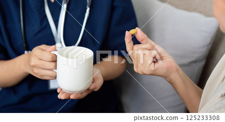 Medication Support and Caregiving. A caregiver assists an elderly patient with their medication, ensuring proper hydration and health management. 125233308