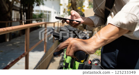Sustainability and Sharing Economy. A person prepares to ride an electric scooter while using his smartphone. Sustainability and Sharing Economy. A person prepares to ride an electric scooter while using his smartphone. 125233349